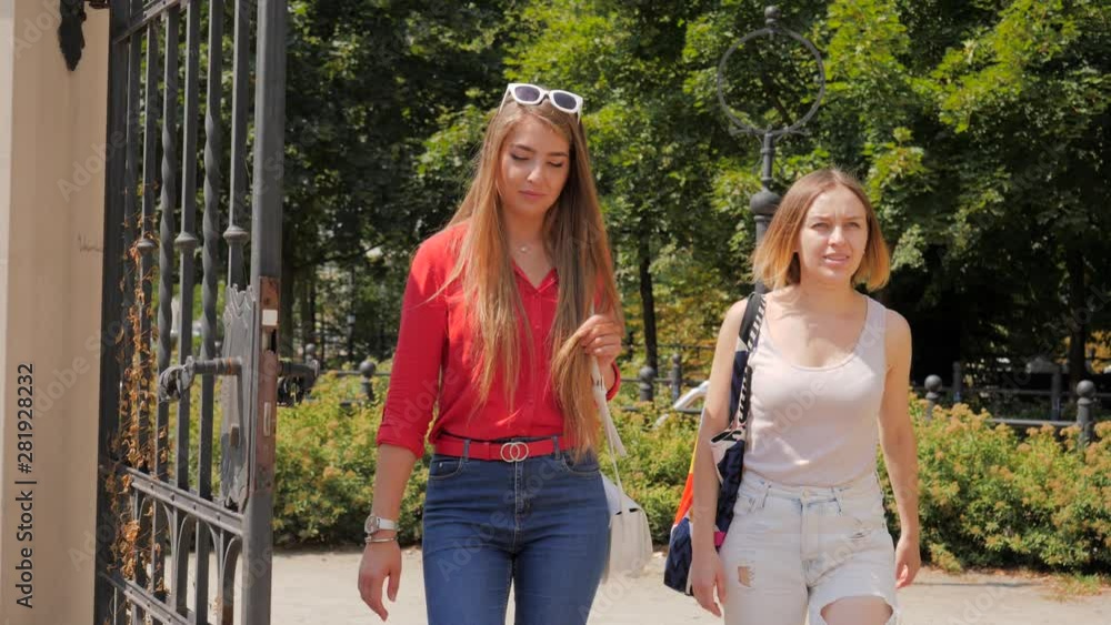 Two young pretty women friends meet and walk together in city communicating Two young pretty women friends meet and walk together in city communicating