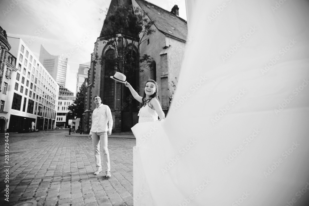 Obraz premium Happy young couple walking near old church in Leipzig. Pregnant woman in beautiful white dress throws up her hat
