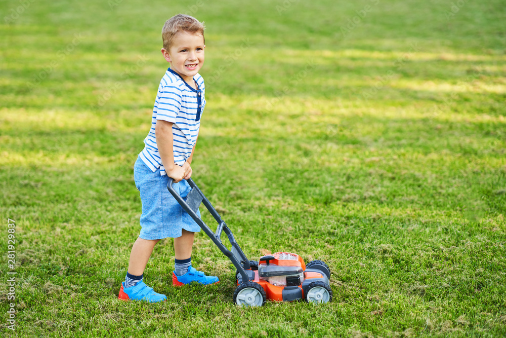 Happy 3 year old boy having fun mowing lawn Happy 3 year old boy having fun mowing lawn