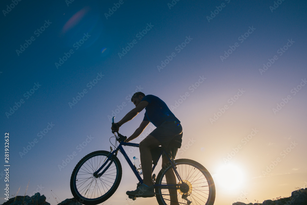 Silhouette of a fit male mountain biker riding his bike uphill on rocky harsh terrain on a sunset. Silhouette of a fit male mountain biker riding his bike uphill on rocky harsh terrain on a sunset.