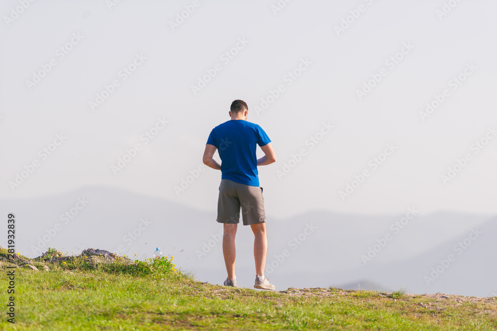 A fit male athlete is preparing for a work out in nature while looking over a cliff at the large lake and mountain line. A fit male athlete is preparing for a work out in nature while looking over a cliff at the large lake and mountain line.