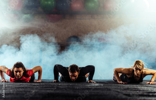 Three bodybuilders doing pushups in gym center photo