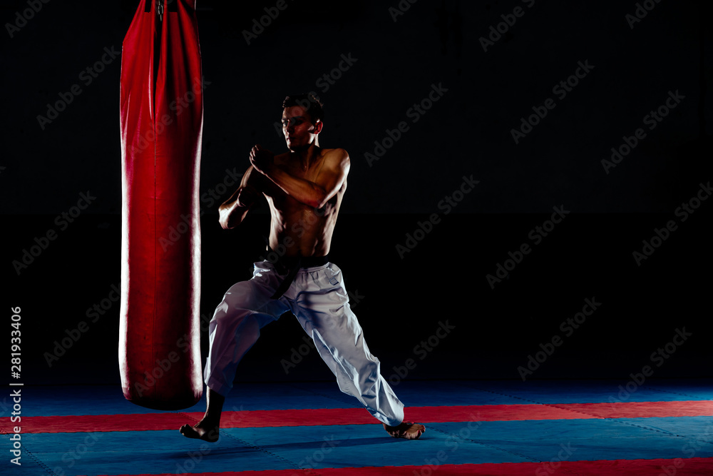 Man practicing boxing on big black bag in gym, low key, high contrast