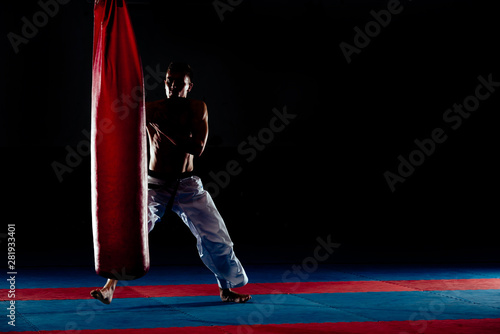 Shirtless sportsman hitting punching bag isolated on black, low key, high contrast