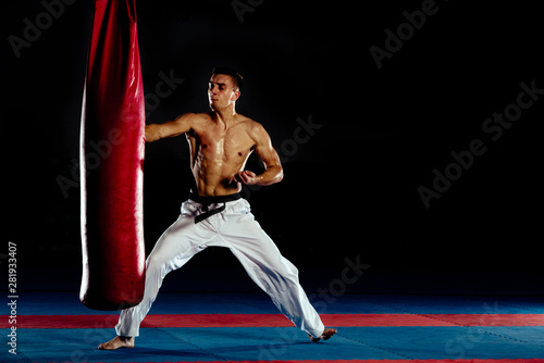 Boxer agressively punching with a kick a sand bag isolated on black wall
