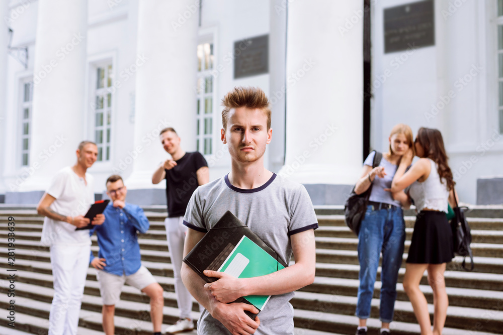 Group of college students standing behind new learner telling gossips, mock, sneer him. Lonely student stands separately from other students because they scoff him and play pranks on him