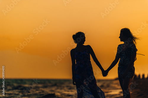 Silhouette of the girls standing at the beach during beautiful sunset