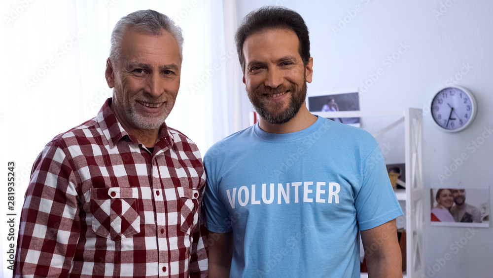 Smiling old male and volunteer looking at camera, charity organization, care Smiling old male and volunteer looking at camera, charity organization, care