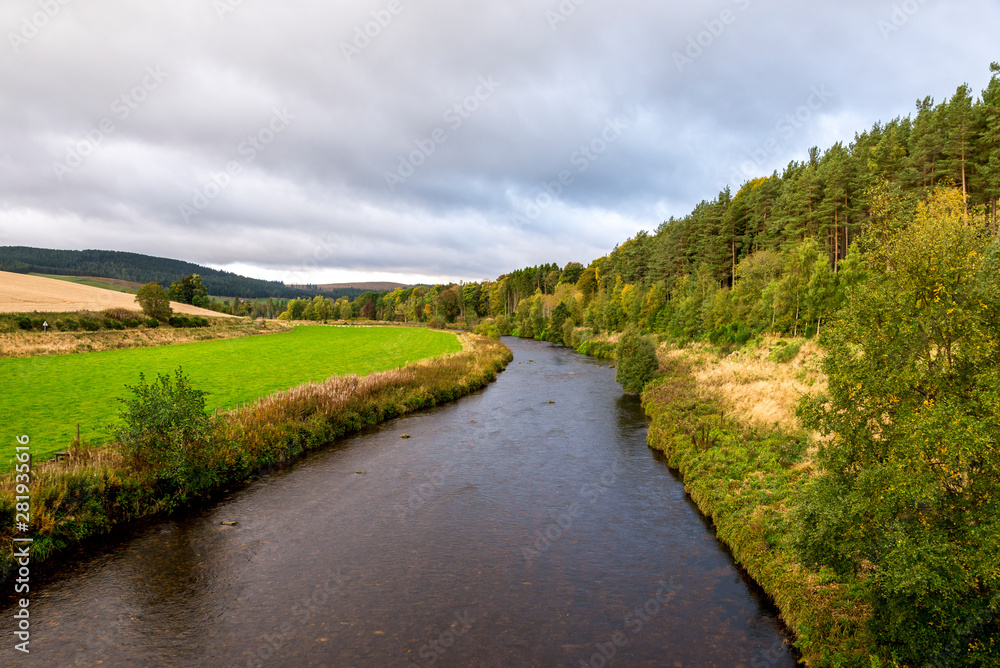A view of the flowing river with a forest on one side and agricultural lands on the other side, autumn in Cairngorms National Park