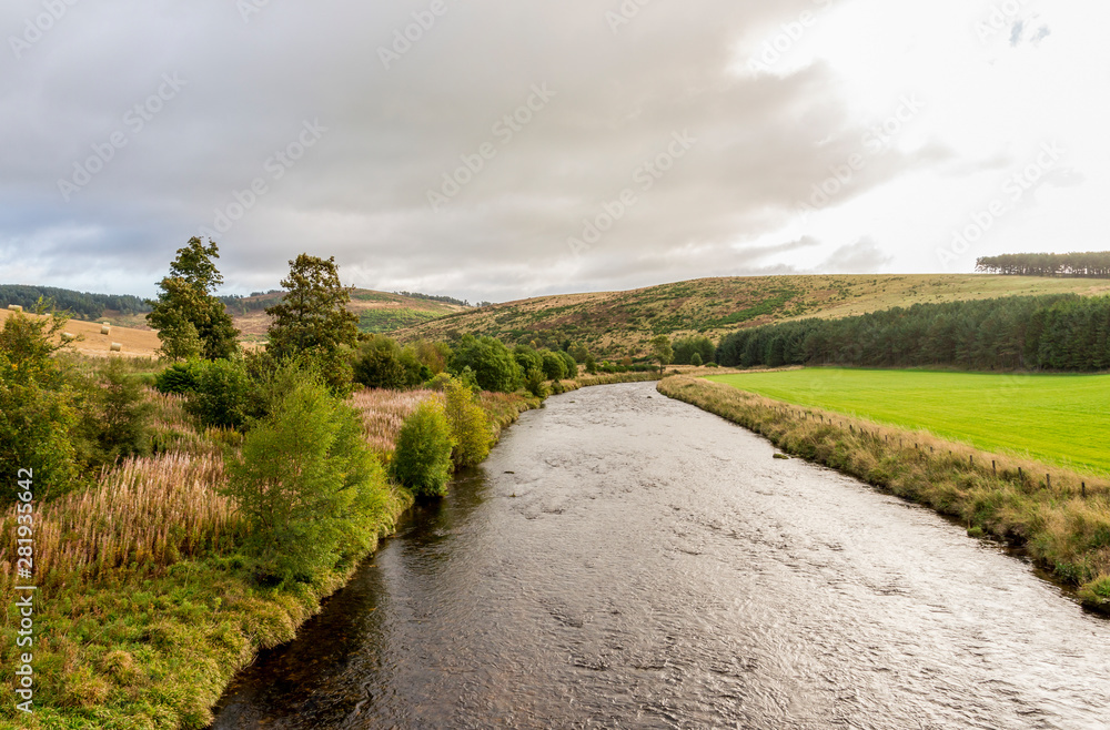 A view of the flowing river and low hills in cloudy weather, autumn in Cairngorms National Park