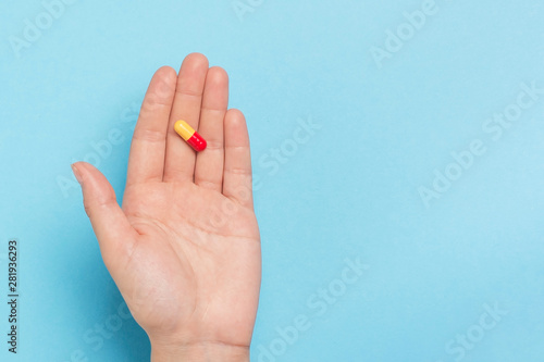 Girl's hand with pill on blue background