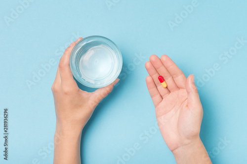 Girl's hands with a glass of water and a pill on a blue background