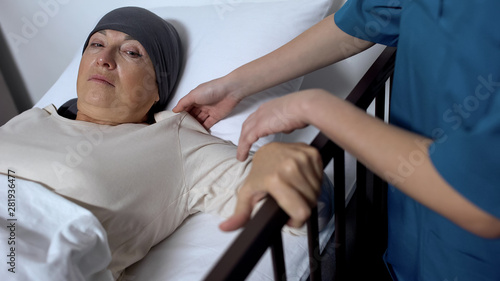 Oncologist helping aged female patient to get out of hospital bed, medic support © motortion