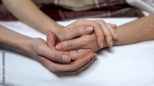 Warm daughters hands holding and calming down sick mother in bed, assistance photo