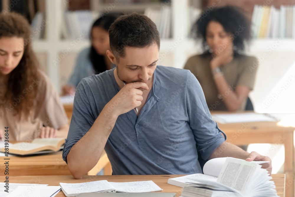 Diverse students absorbed reading textbook studying sitting at desks Diverse students absorbed reading textbook studying sitting at desks