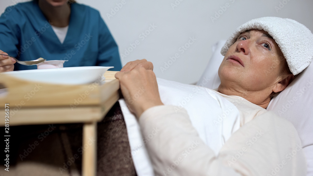 Obraz premium Sick-nurse feeding disabled woman with compress on forehead, hopelessness