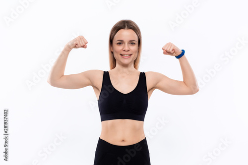 Young sporty blond woman in a black sportswear showing biceps standing over white background.