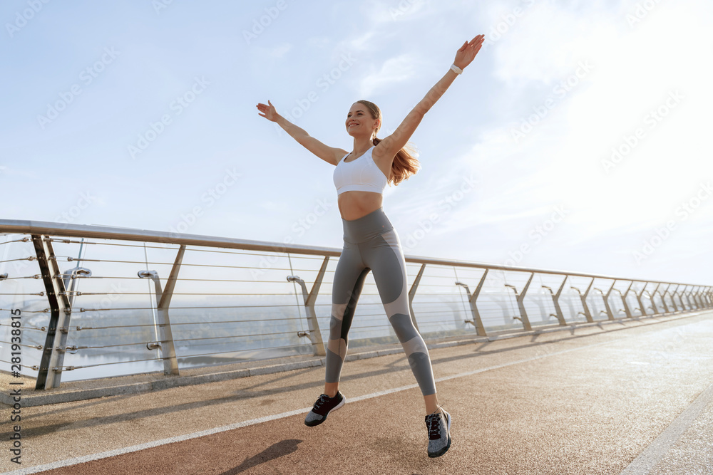Obraz premium Sportive happy lady jumping up on foot bridge