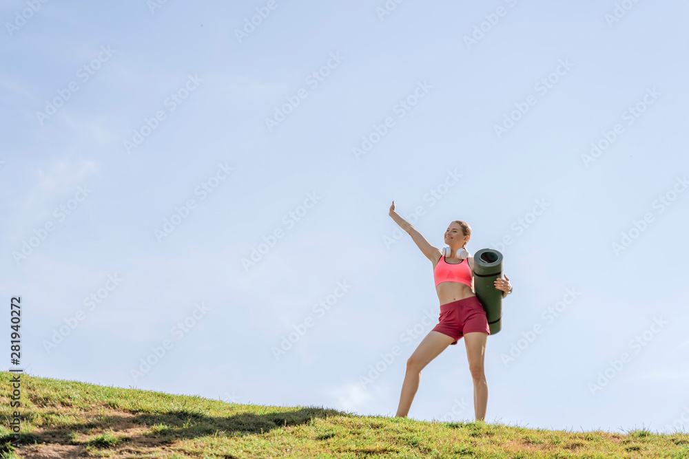 Sportive happy lady staying on green hill with mat Sportive happy lady staying on green hill with mat