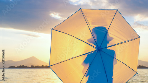 Silhouette of young boy hipster in hat with umbrella. Kid with umbrella looking at seascape. Travelling concept. Summer holidays background. Goodbye summer. Farewell to summer. Incognito background