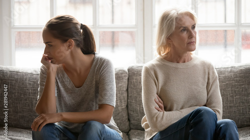 Elderly mother and grown up daughter sit on couch separately