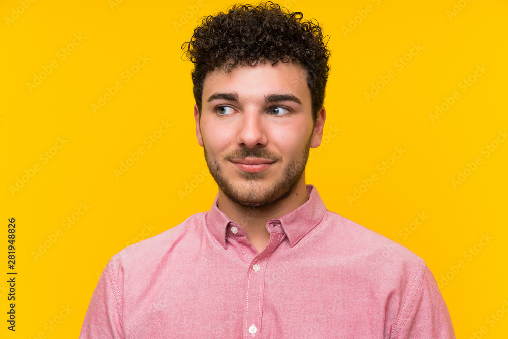 Man with curly hair over isolated yellow wall standing and looking to the side Man with curly hair over isolated yellow wall standing and looking to the side