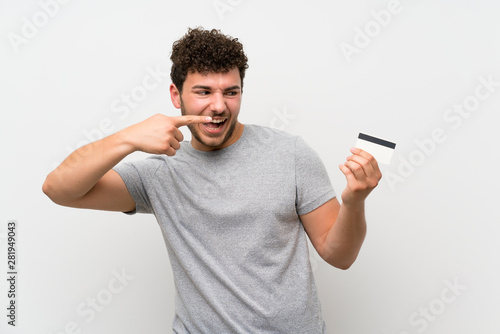 Man with curly hair over isolated wall holding a credit card