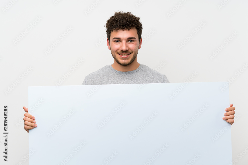 Man with curly hair over isolated wall holding an empty white placard for insert a concept Man with curly hair over isolated wall holding an empty white placard for insert a concept