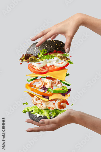 Flying burger with fresh ingredients between woman's hands on a light background. photo