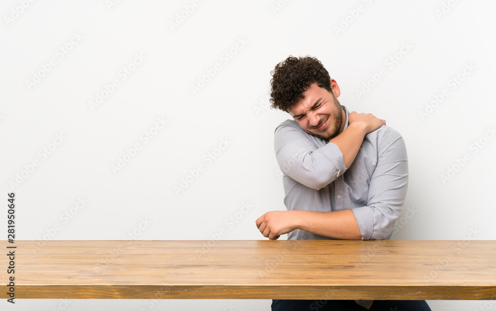 Young man with a table suffering from pain in shoulder for having made an effort Young man with a table suffering from pain in shoulder for having made an effort