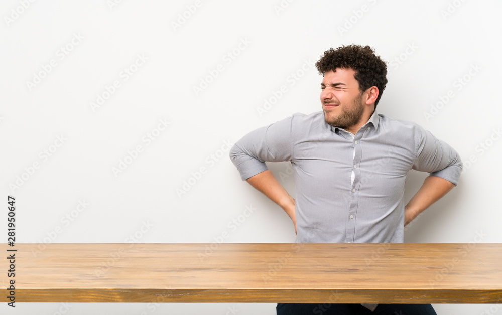 Young man with a table suffering from backache for having made an effort Young man with a table suffering from backache for having made an effort