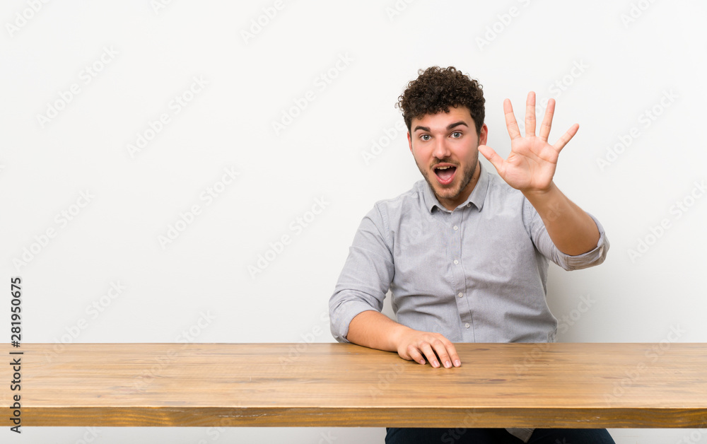 Young man with a table counting five with fingers Young man with a table counting five with fingers