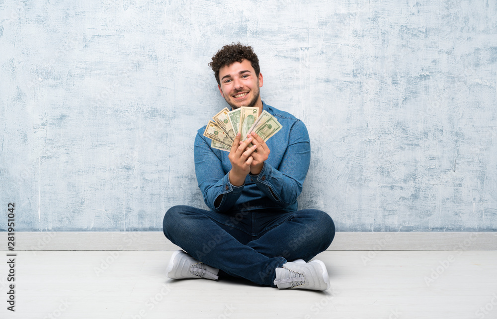 Young man sitting on the floor taking a lot of money Young man sitting on the floor taking a lot of money