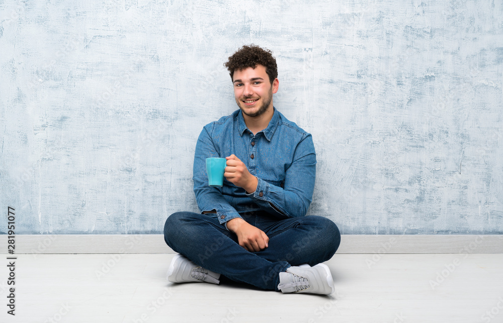 Young man sitting on the floor holding hot cup of coffee