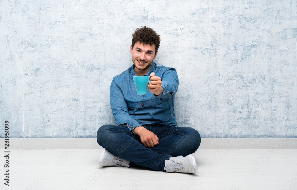 Young man sitting on the floor holding hot cup of coffee