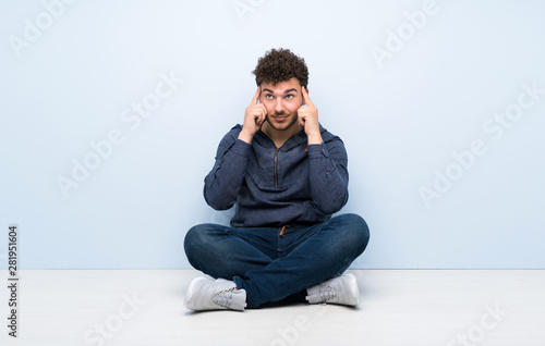 Young man sitting on the floor having doubts and thinking © luismolinero
