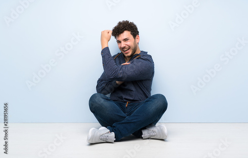 Young man sitting on the floor doing strong gesture © luismolinero