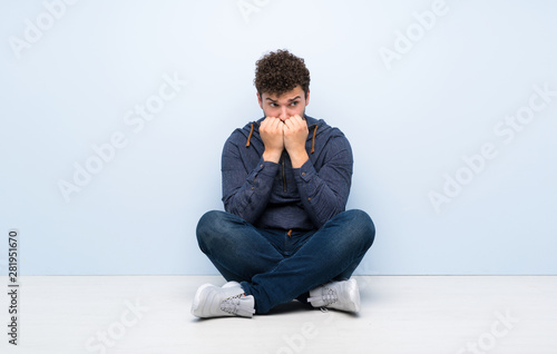 Young man sitting on the floor nervous and scared putting hands to mouth © luismolinero