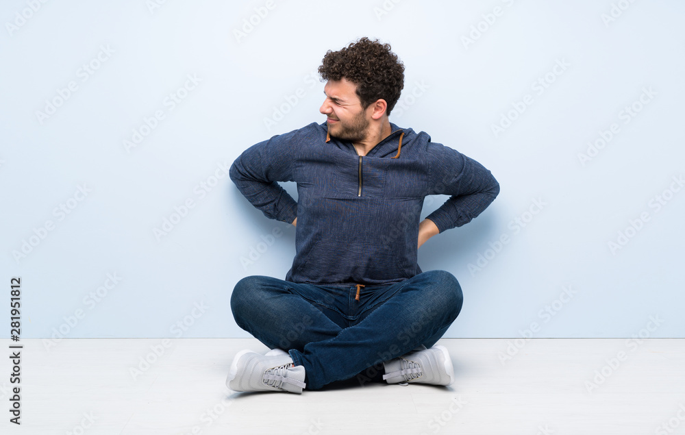 Young man sitting on the floor suffering from backache for having made an effort Young man sitting on the floor suffering from backache for having made an effort