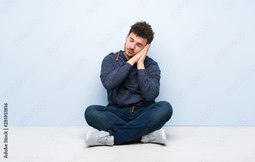 Young man sitting on the floor making sleep gesture in dorable expression Young man sitting on the floor making sleep gesture in dorable expression