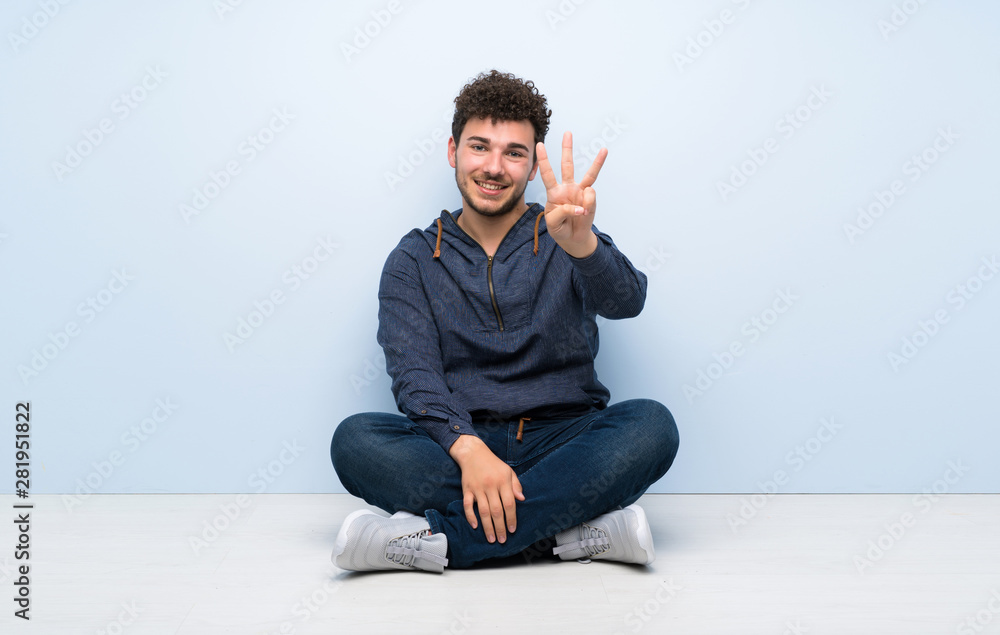 Young man sitting on the floor happy and counting three with fingers Young man sitting on the floor happy and counting three with fingers