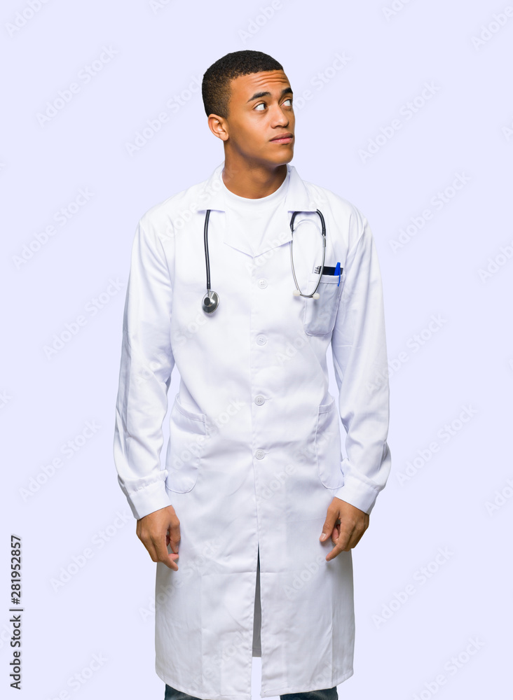 Young afro american man doctor looking up with serious face on isolated background Young afro american man doctor looking up with serious face on isolated background