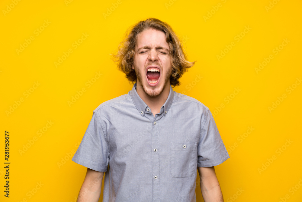 Blonde man over isolated yellow background shouting to the front with mouth wide open Blonde man over isolated yellow background shouting to the front with mouth wide open