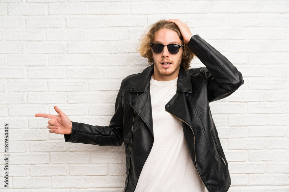 Blonde man with sunglasses surprised and pointing finger to the side Blonde man with sunglasses surprised and pointing finger to the side