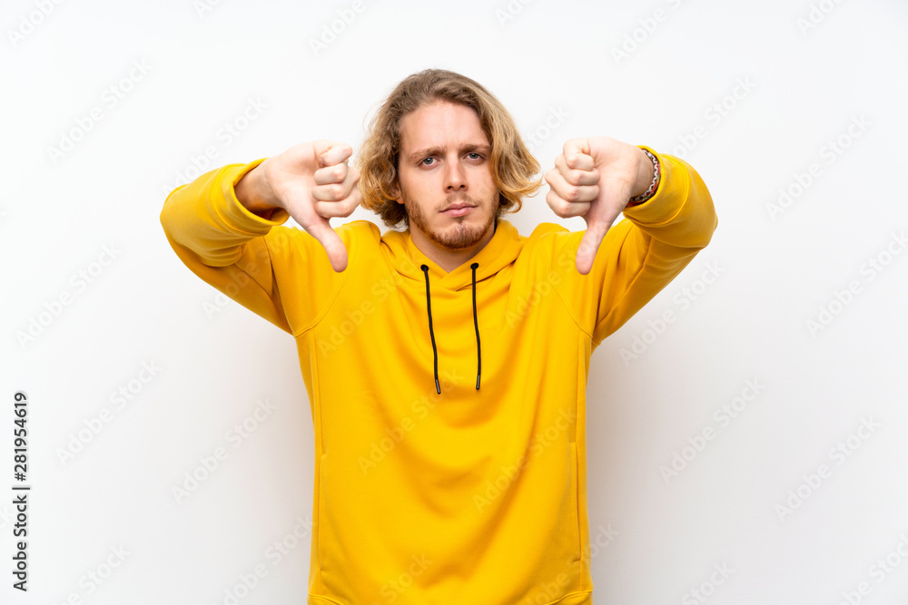 Naklejka premium Blonde man with sweatshirt over white wall showing thumb down