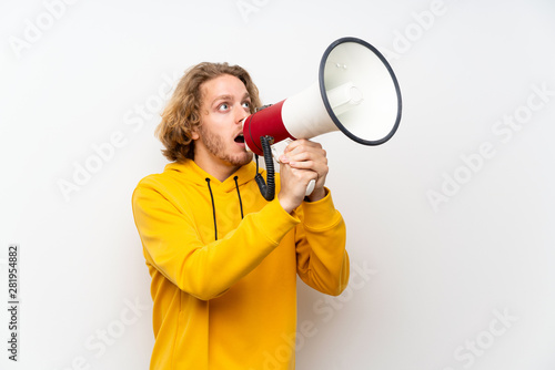 Blonde man with sweatshirt over white wall shouting through a megaphone