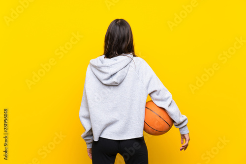 Young woman playing basketball over isolated yellow background