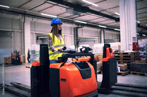 Industrial worker in protective uniform with hardhat operating forklift in big warehouse distribution center. Warehouse worker organizing unloading.