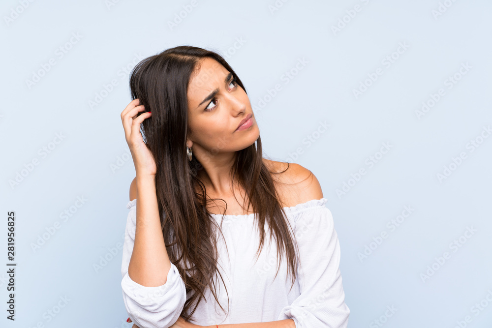 Young woman over isolated blue background having doubts and with confuse face expression Young woman over isolated blue background having doubts and with confuse face expression