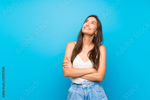 Young woman over isolated blue background looking up while smiling © luismolinero